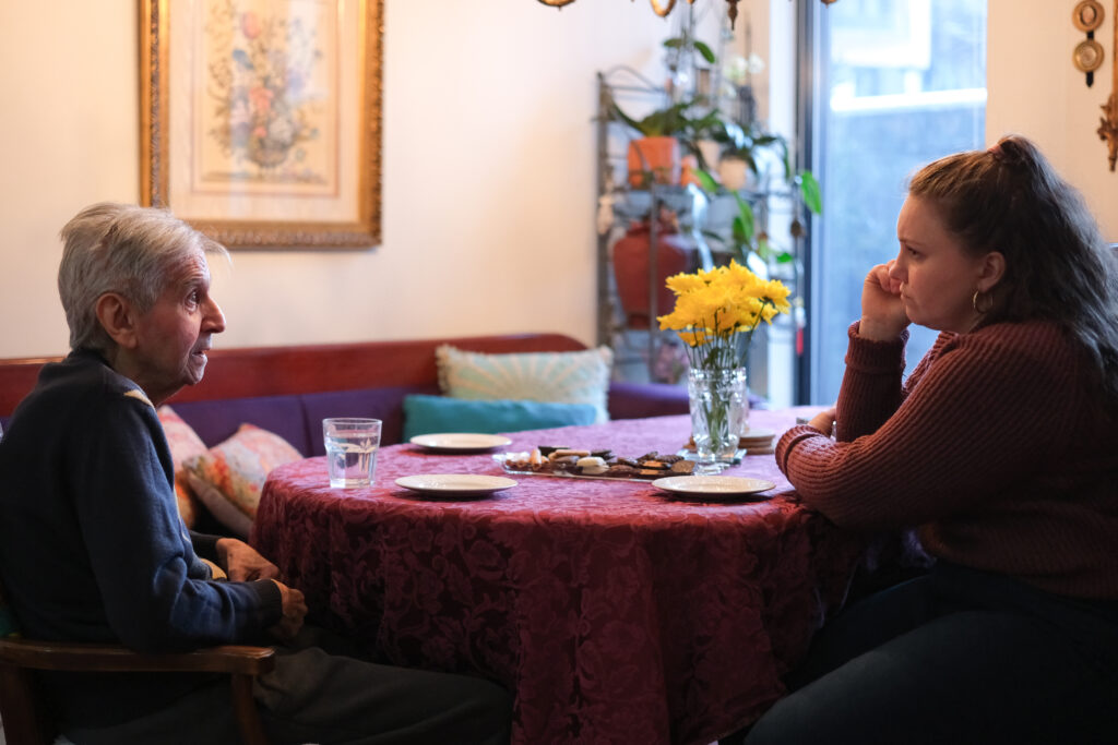 A young woman and a senior man sit across each other at a table.